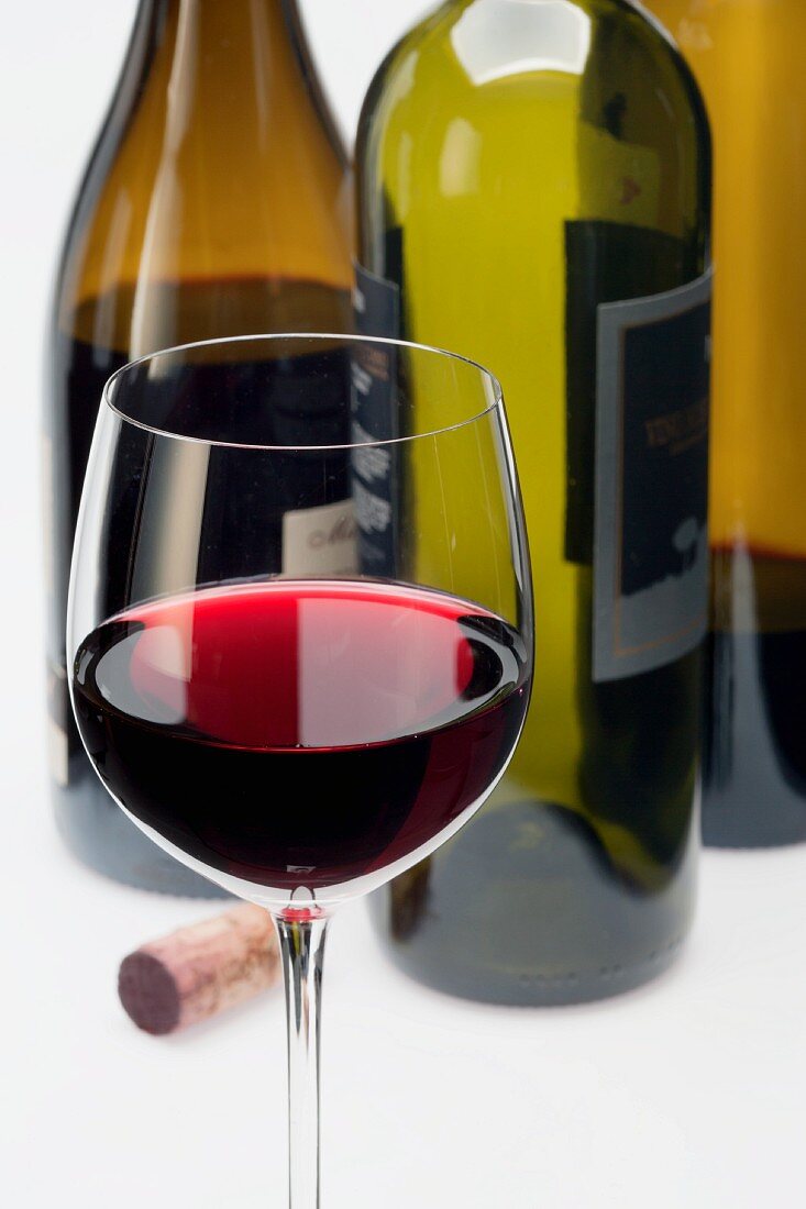 Ein Glas Rotwein und Korken vor Weinflaschen