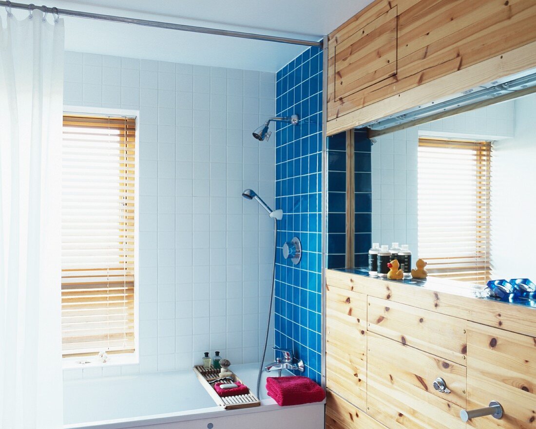 Schlichtes Bad mit farbigen Wandfliesen über Badewanne und Spiegel in Nische mit Holzverkleidung