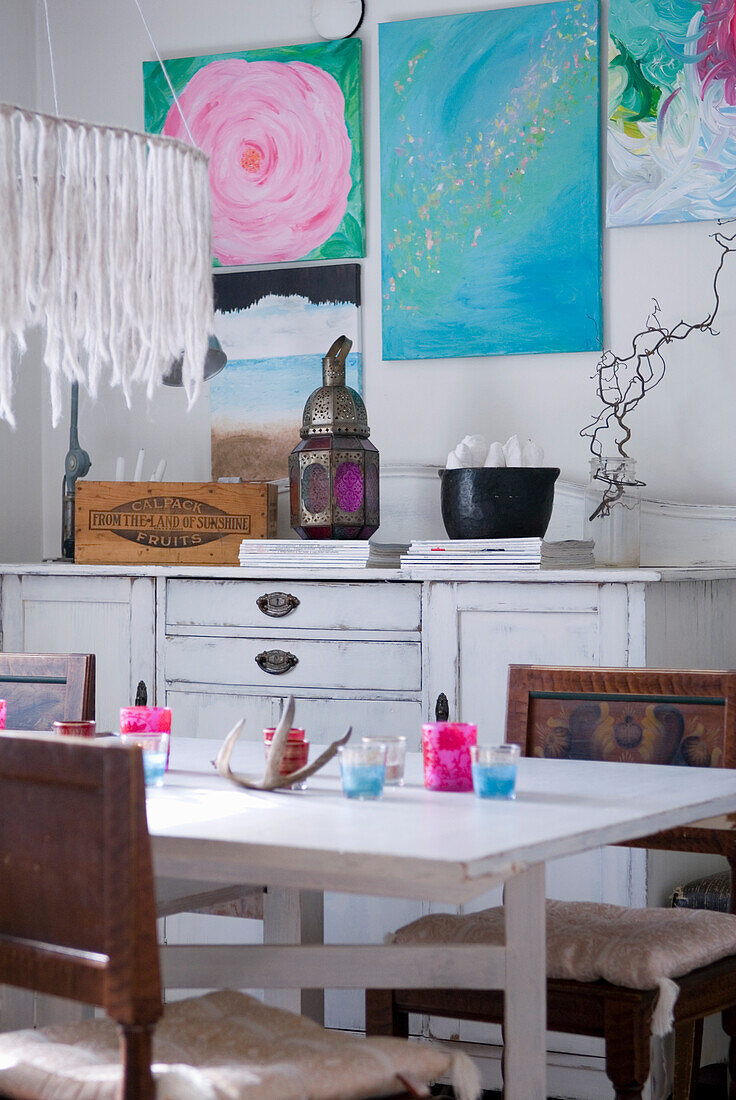 White dining table with chairs and colorful wall art in a living room