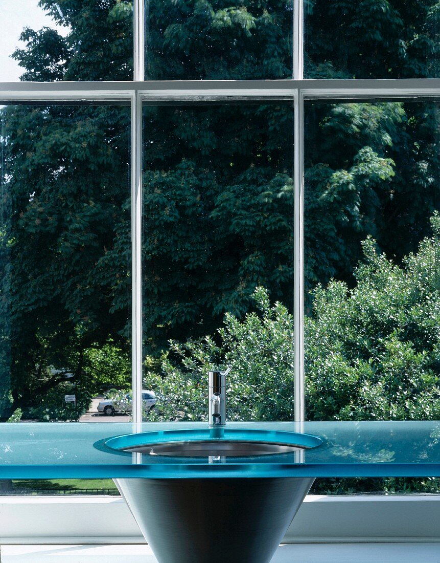Designer washstand with blue glass slab in front of lattice window with view of trees