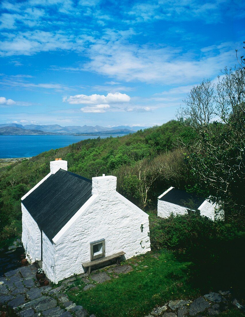 Old, Irish farmhouse with gable-end chimneys on green hill with expansive view