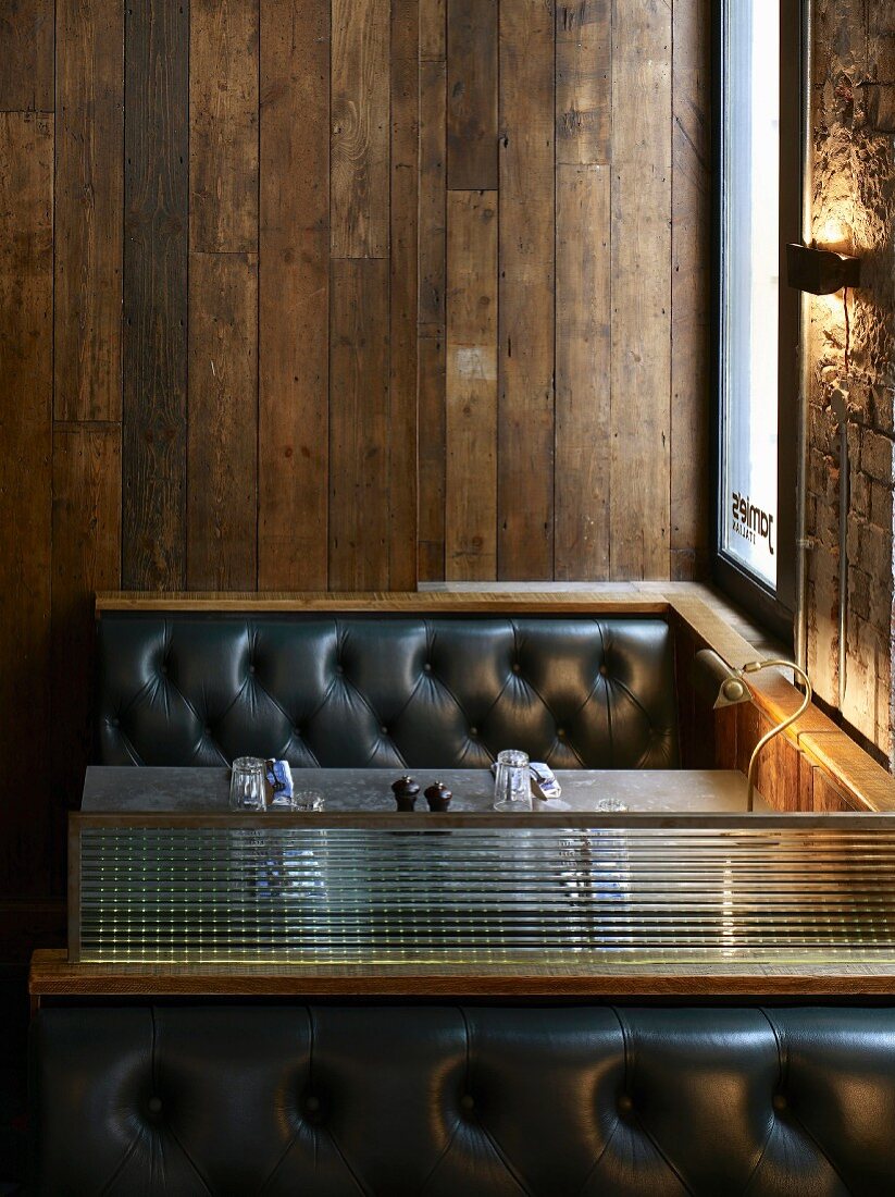 Vintage-look booths - benches with black leather upholstery and brass-coloured retro lamp in front of old wooden wall