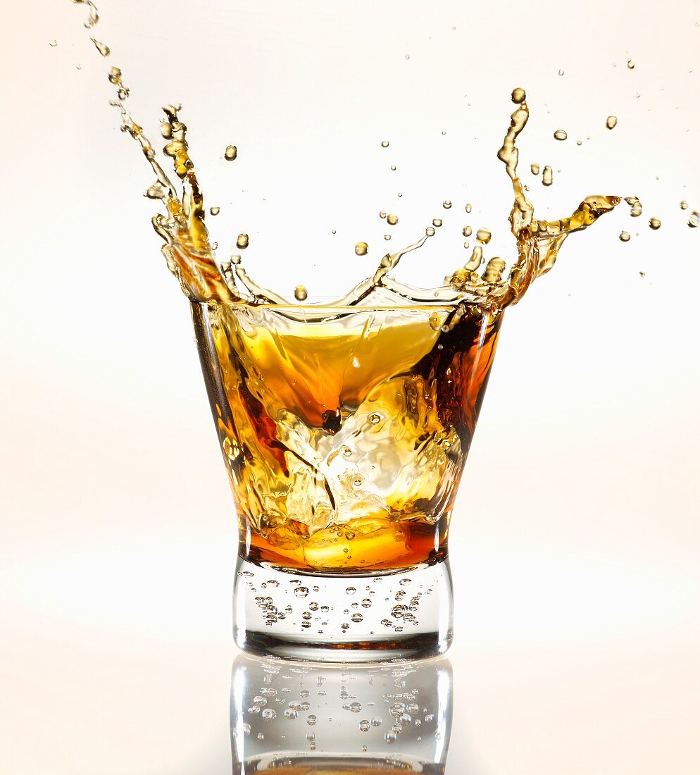 Eiswürfel fällt in ein Glas Scotch