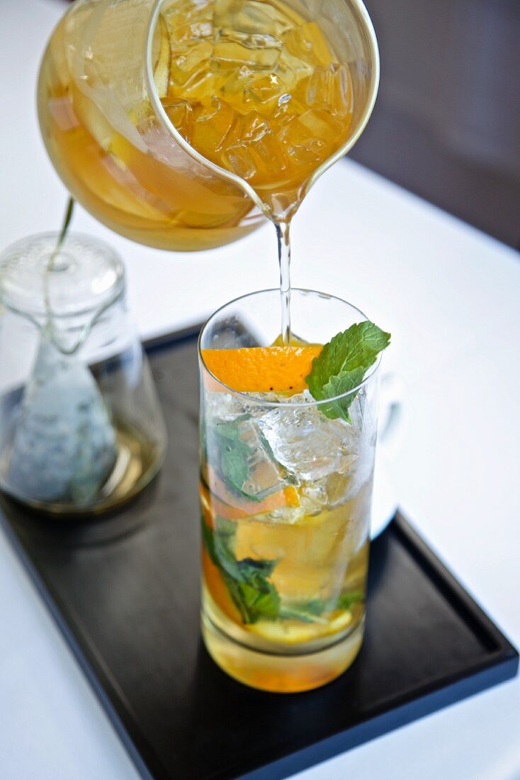 Orange, Pear and Mint Iced Tea Pouring From a Pitcher into a Glass