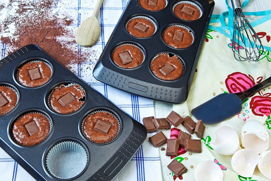 Unbaked chocolate muffins in muffin tins with chocolate pieces in the middle