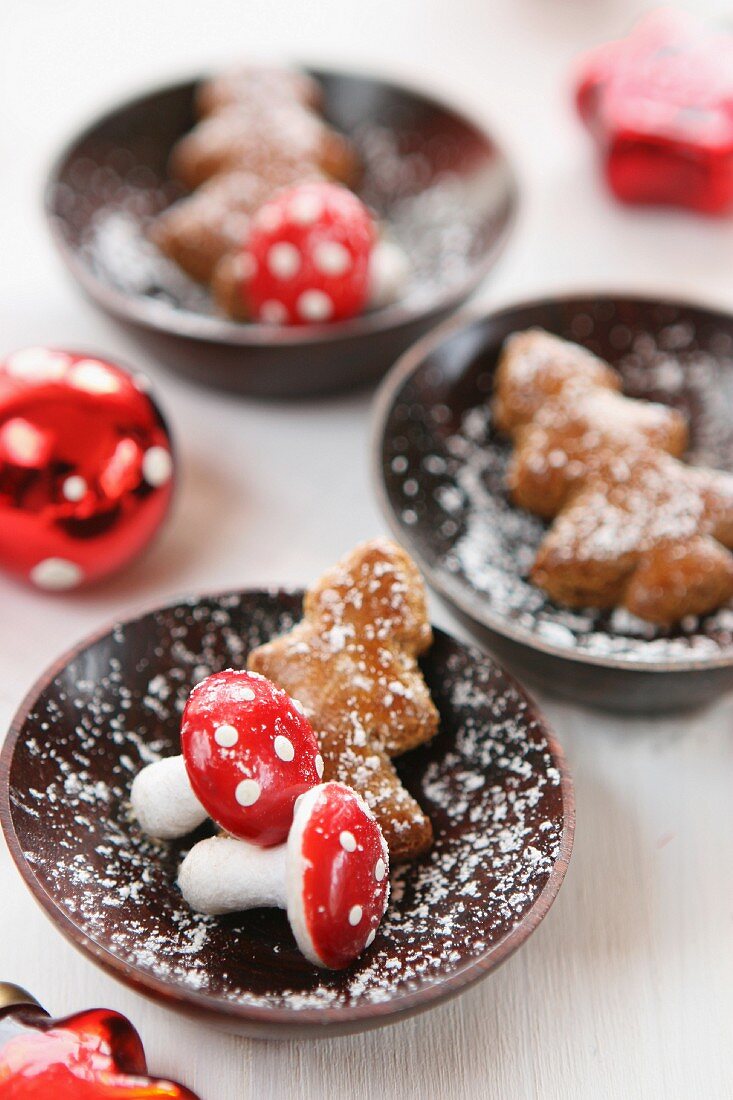 Mini gingerbread Christmas trees and decorative toadstools in wooden bowls dusted with icing sugar