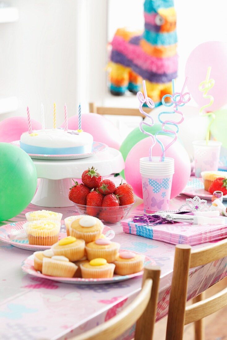 Fairy cakes, fresh strawberries and a birthday cake for children on a table with party decorations