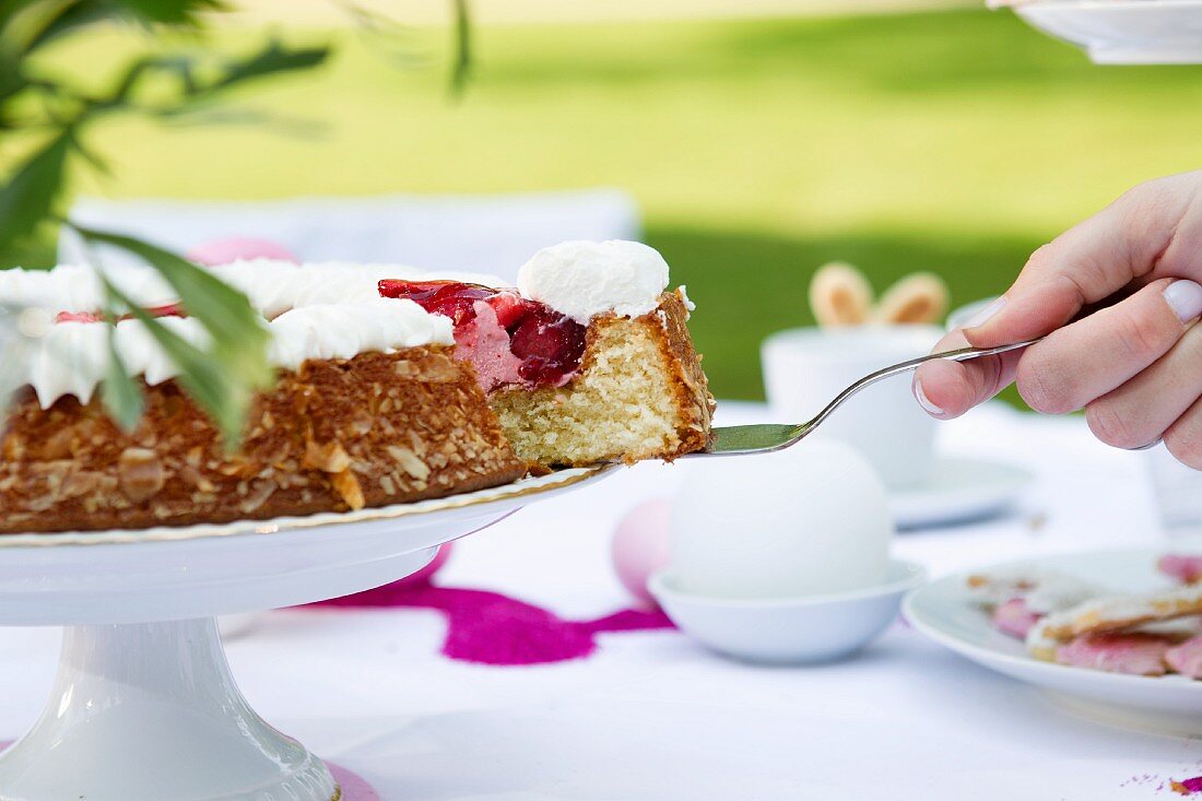 A hand taking a slice of strawberry cake with a cake slice