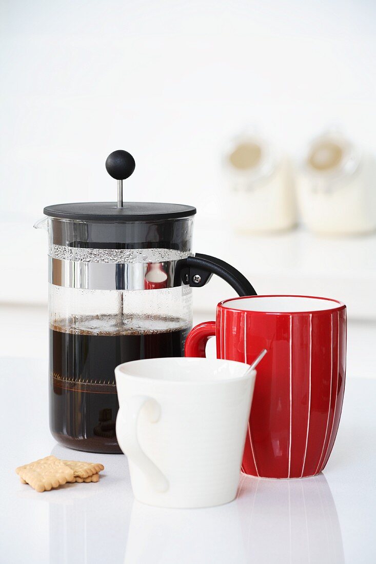 Kaffee in einer Kanne, ein roter Becher und eine weiße Tasse