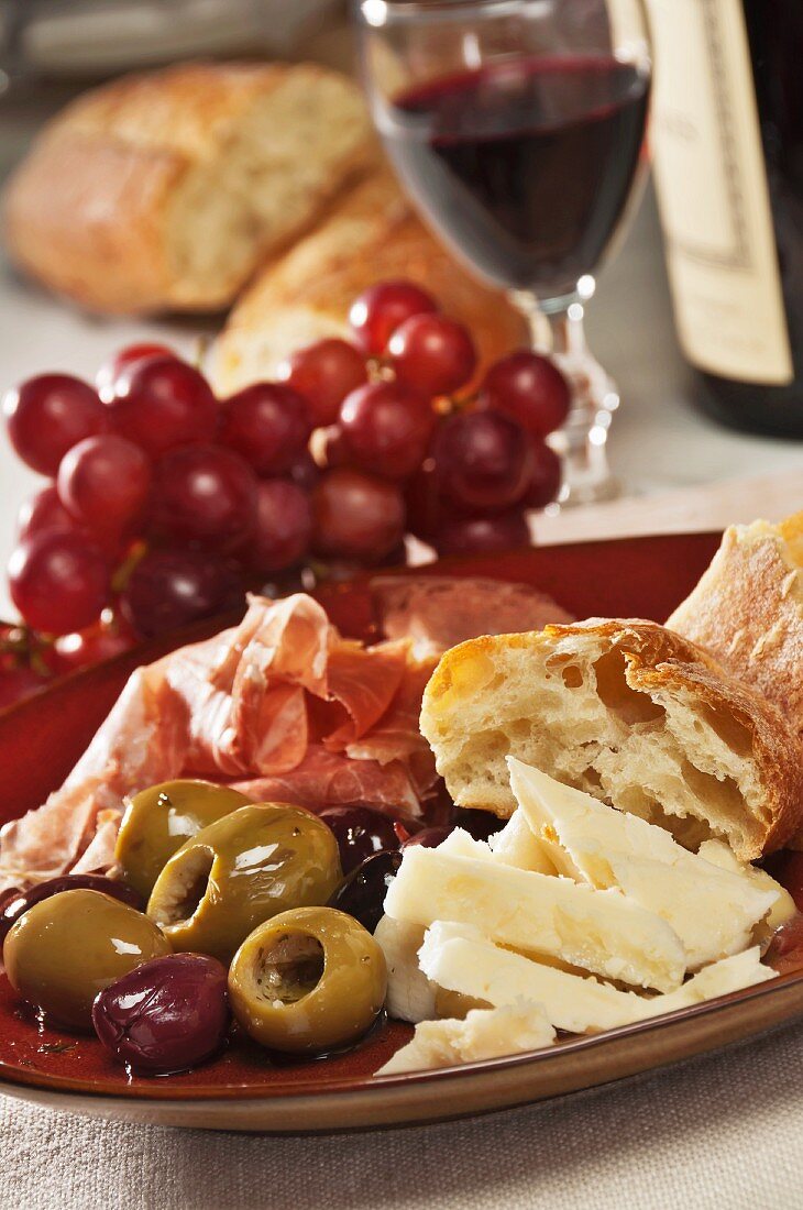 Antipastiteller mit Provolone, Prosciutto, Oliven, Ciabatta, Trauben und Rotwein