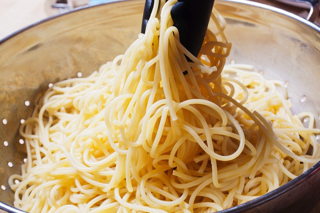 Gekochte Spaghett mit einer Zange aus dem Sieb heben