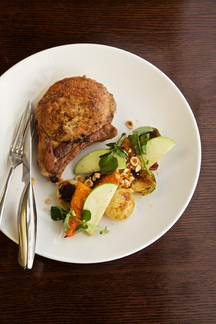 Pork Chop with Veggies and Apple Slices; On a White Plate with Fork and Knife