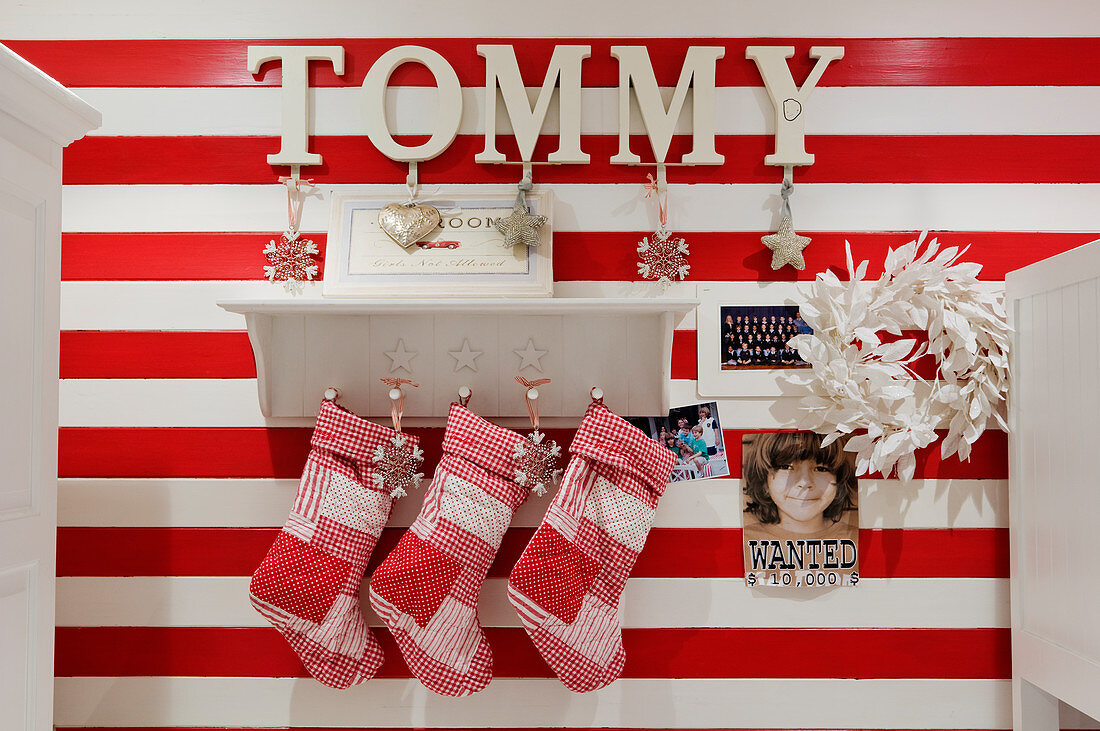 Christmas stockings hanging from traditional bracket shelf on red and white striped wall