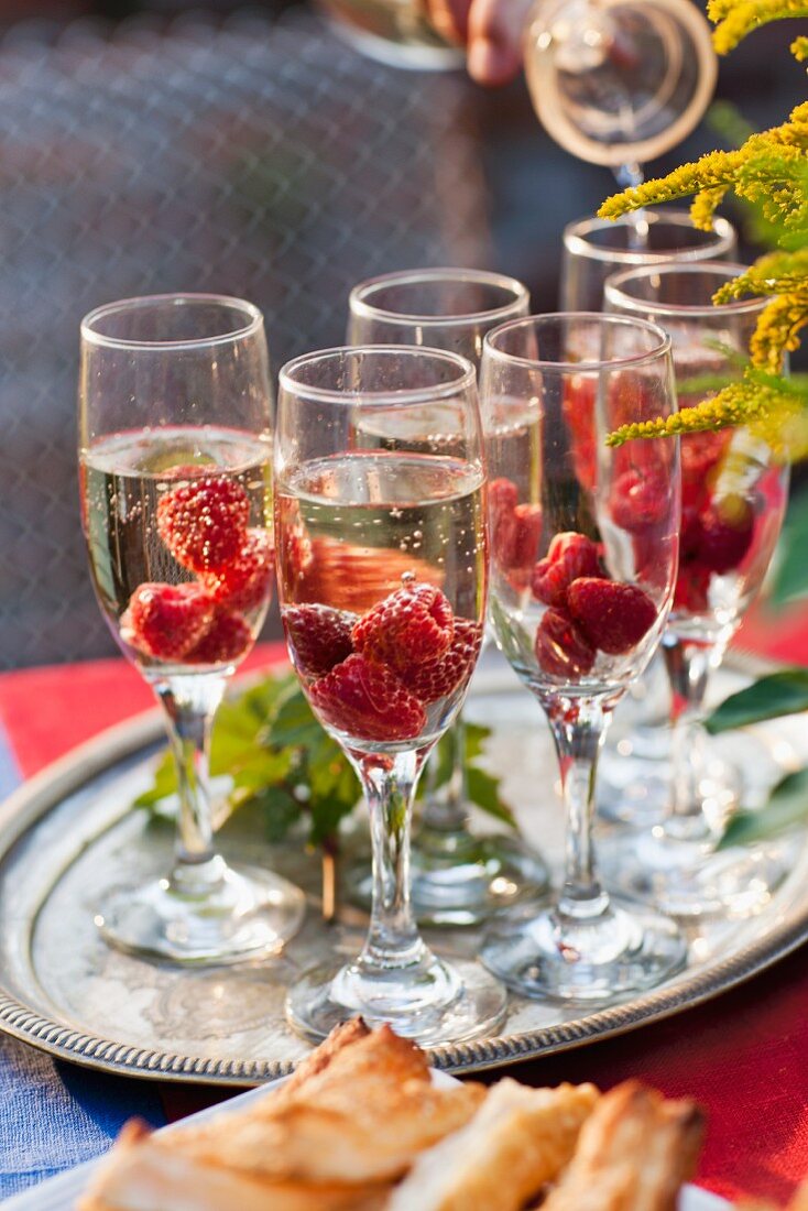 Sparkling wine with raspberries in several glasses on buffet table