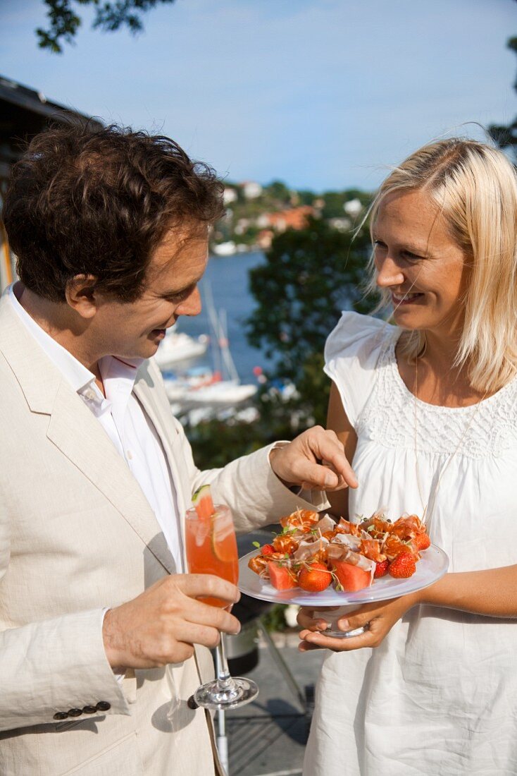 Couple with fruit skewers and a melon drink at a summer party