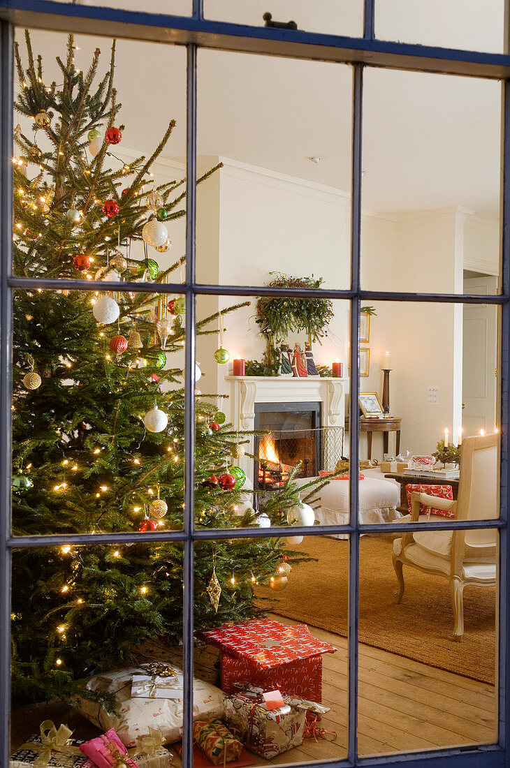 Blick durch Sprossenfenster auf geschmückten Weihnachtsbaum in traditionellem Ambiente
