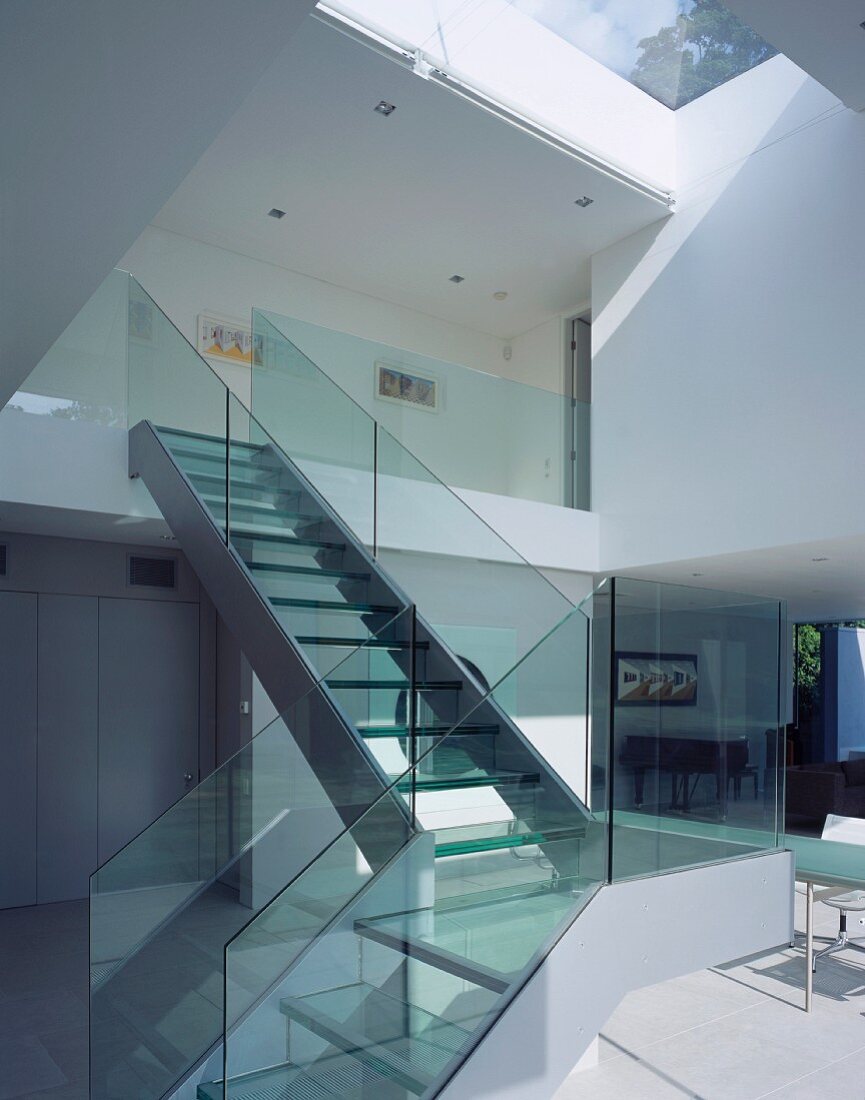 Staircase with glass balustrade leading from living space to upper storey
