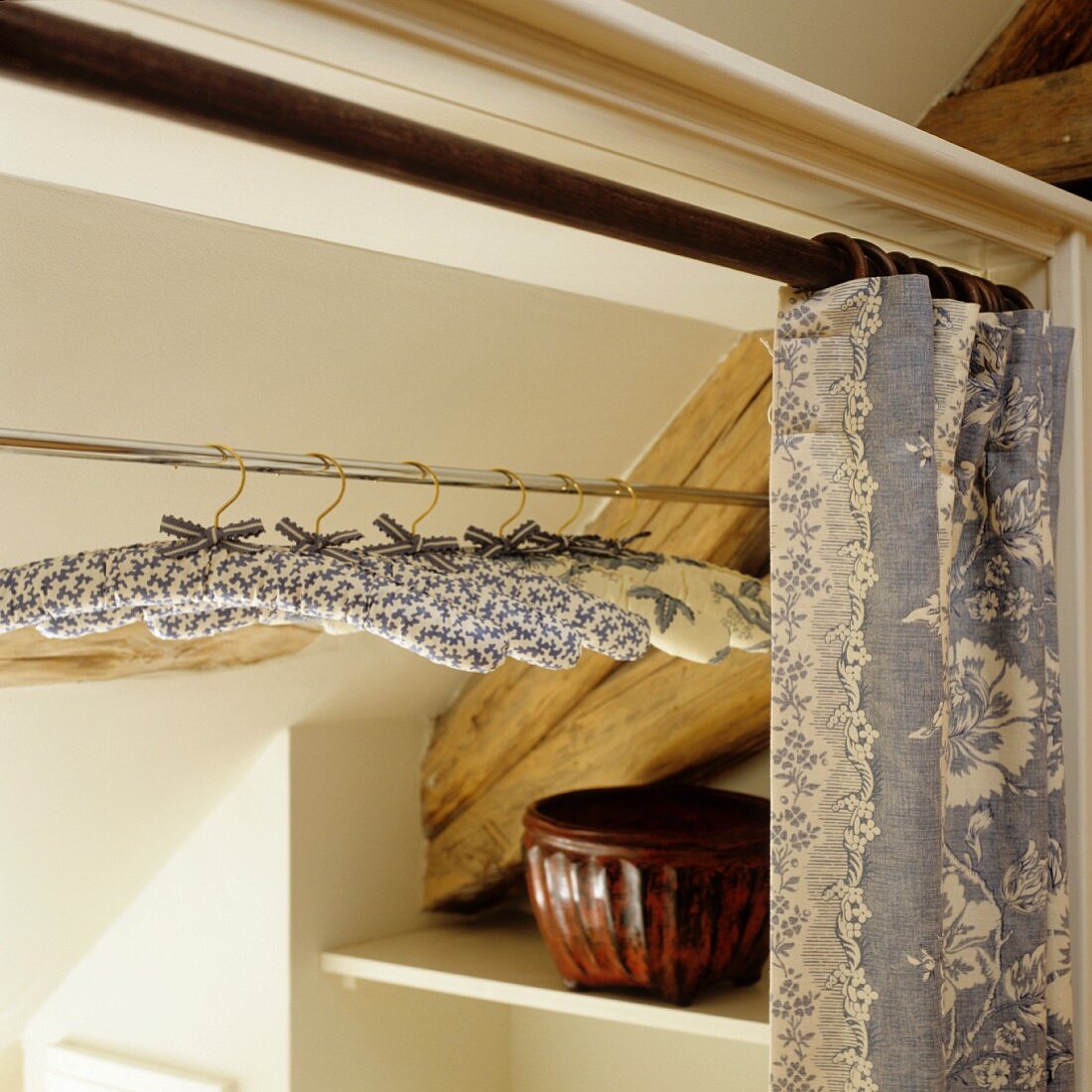 Mit Stoff bezogene Kleiderbügel auf Kleiderstange hinter offenem Vorhang