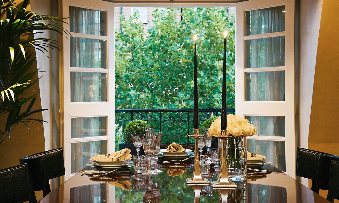 Festive table with candle sticks in front of open balcony doors