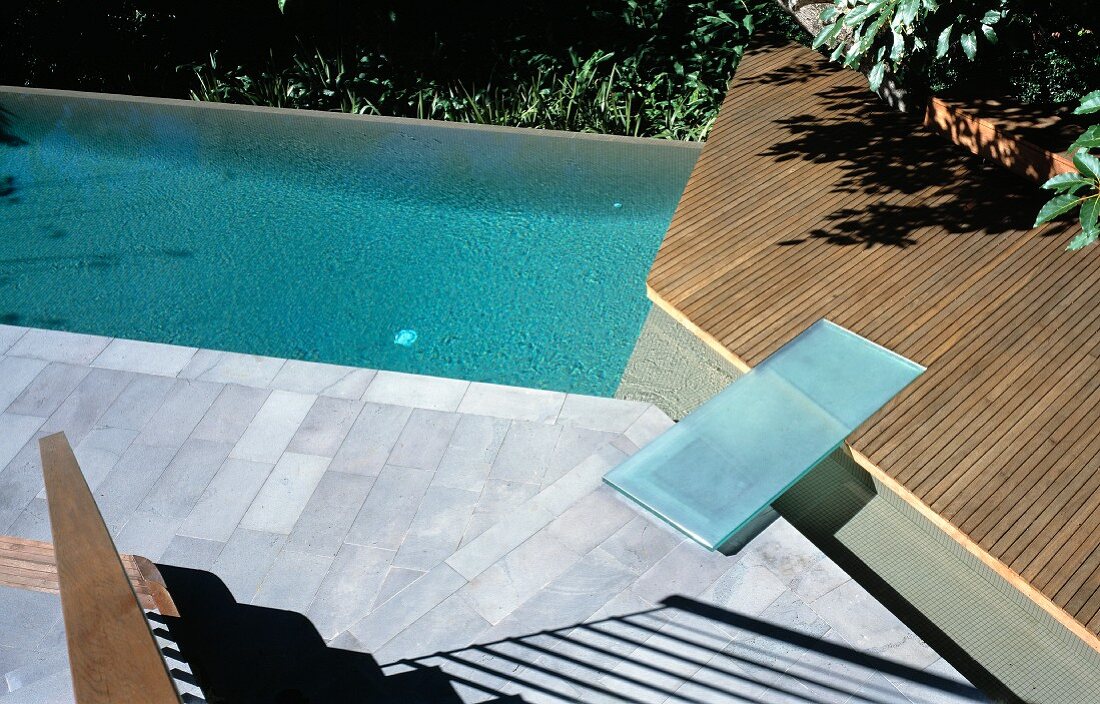 Footbridge made of glass slab connecting two terraces next to swimming pool