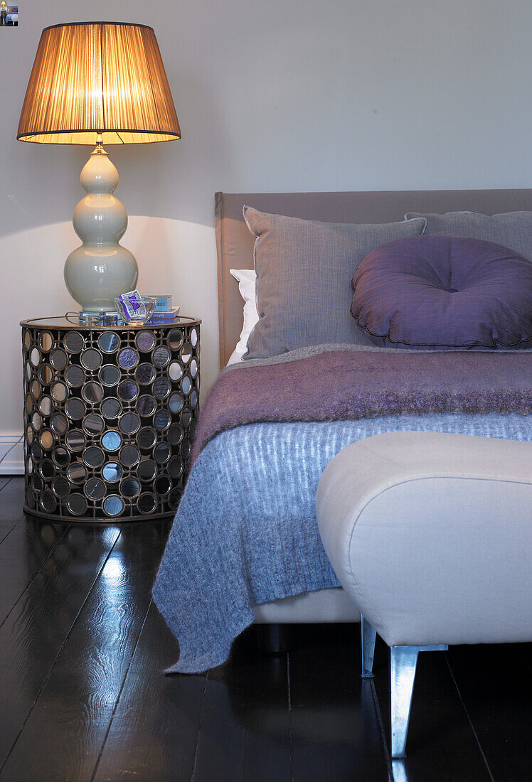 Bedside table with lamp next to bed in shades of purple, blue and grey