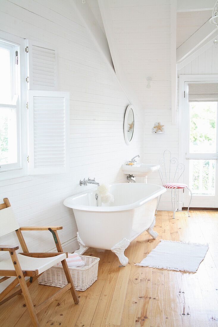 Freestanding bathtub in light-coloured bathroom with wooden floor