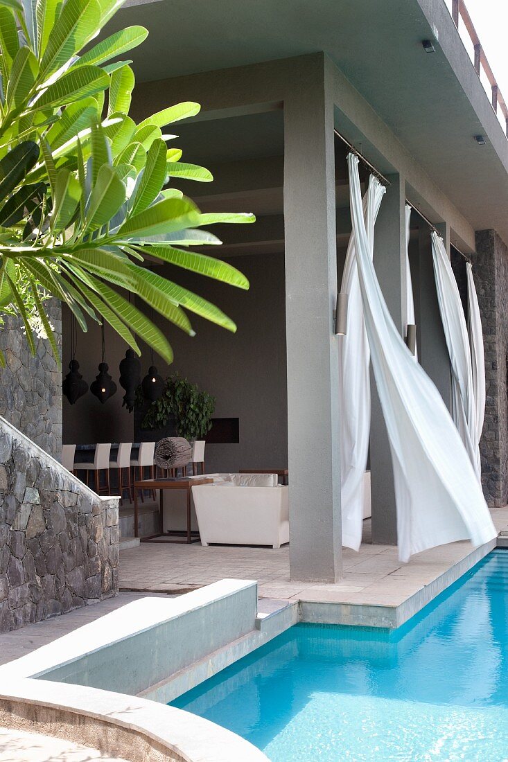 Roofed terrace with billowing curtains next to pool