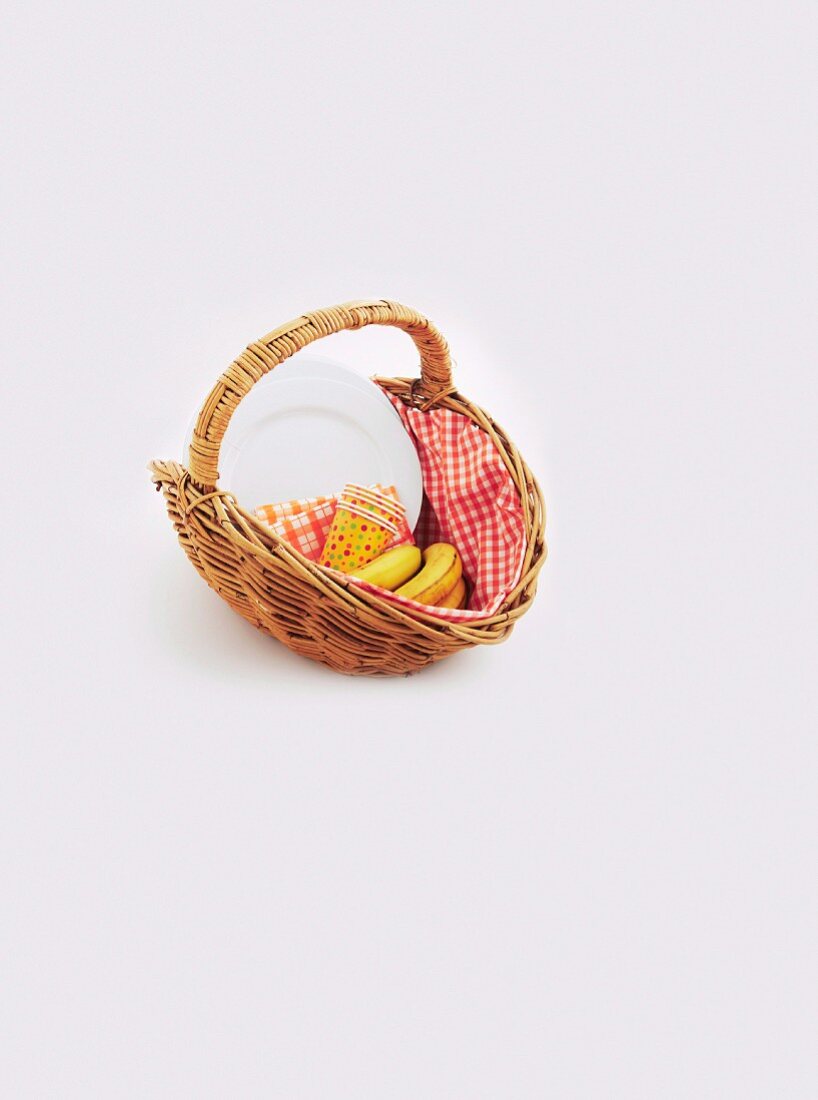 A wicker basket with bananas, paper cups, napkins and plates