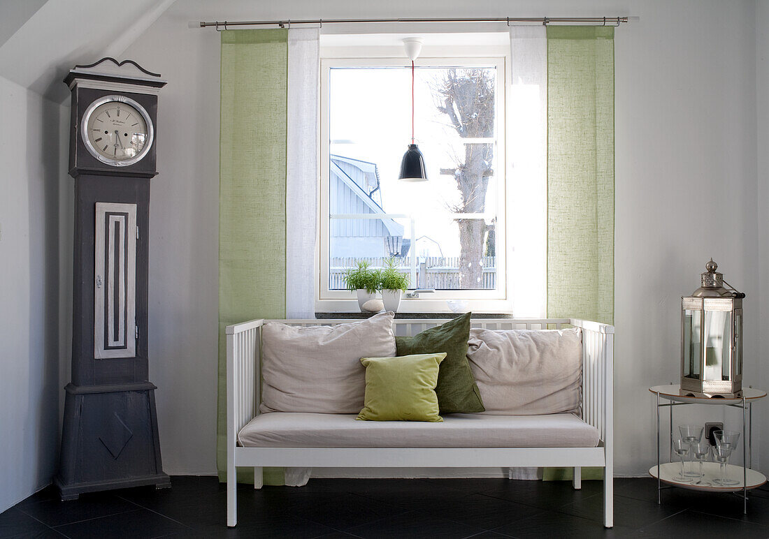 White bench with cushions in front of window, grandfather clock