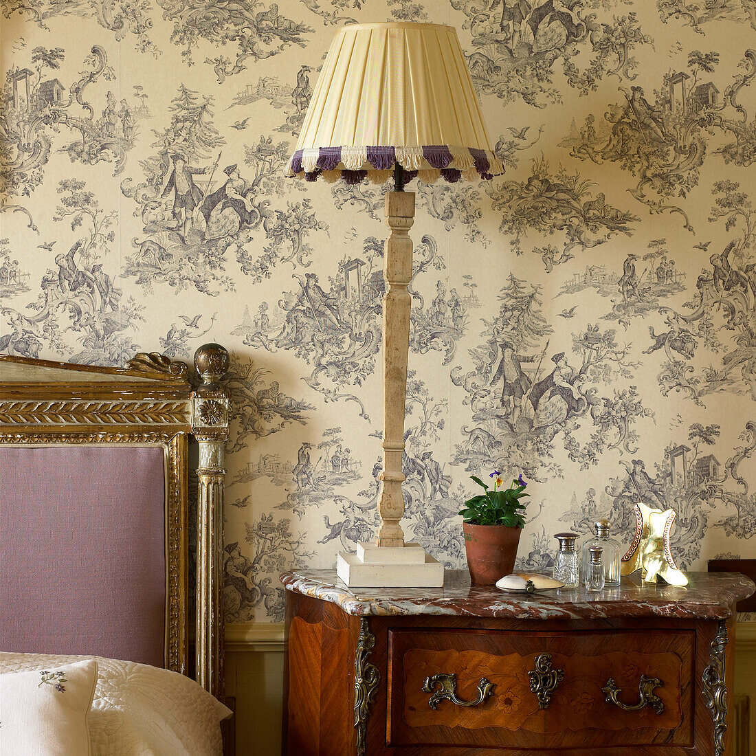 Table lamp on antique chest of drawers, wallpaper in Toile de Jouy style