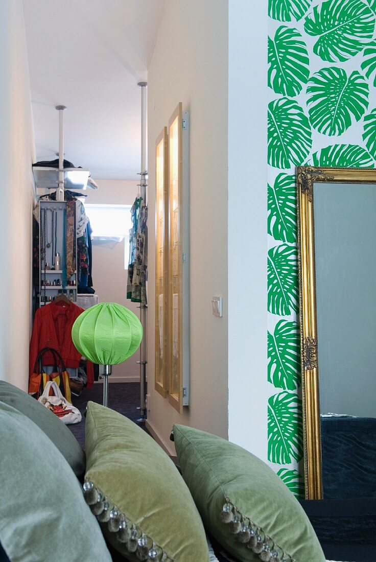 A view of a walk-in wardrobe in a bedroom featuring a multitude of styles including palm leaf wallpaper and velvet cushions in the foreground