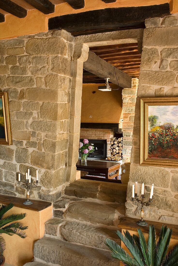 Stone staircase to a rustic living room with open fireplace and wood pile