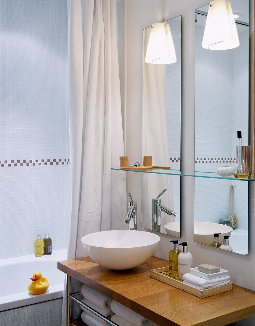 White basin on wooden surface in front of mirror in modern bathroom
