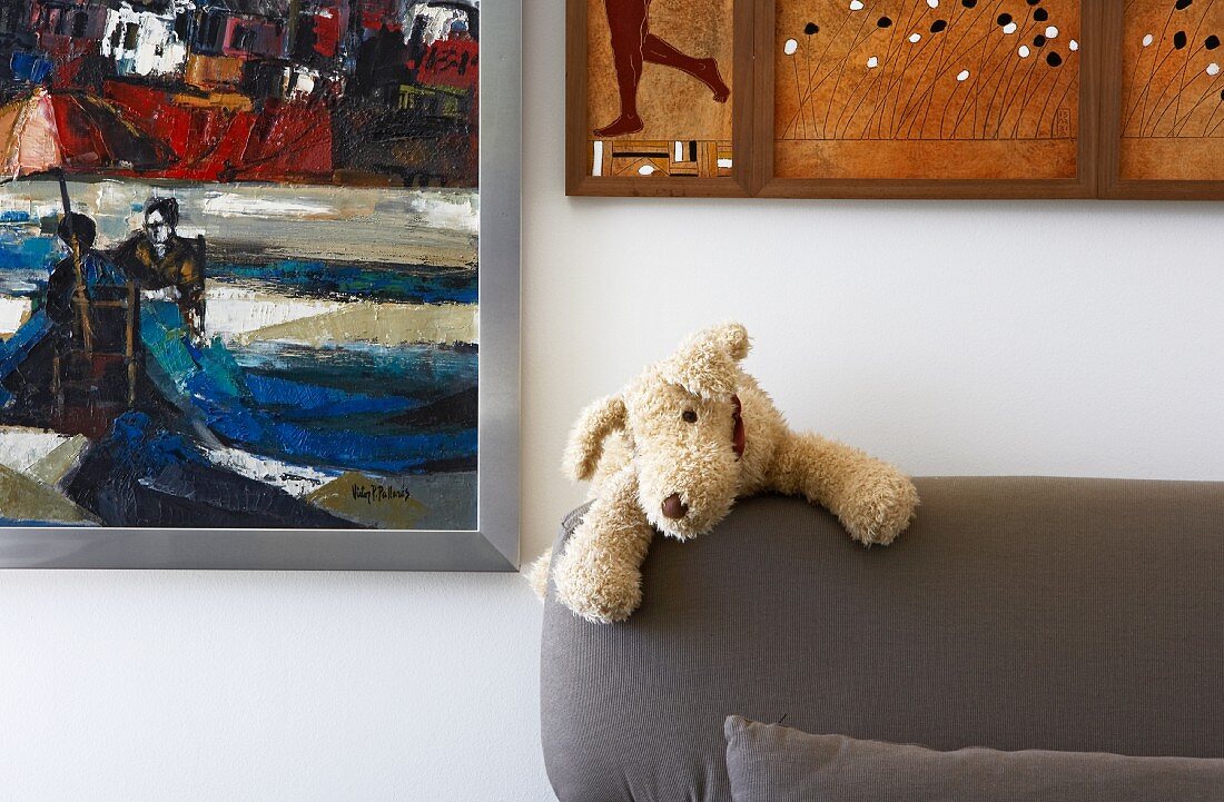 Kleiner Stoffhund auf der Rückenlehne eines Polstersofas und verschiedene Gemälde an der Wand