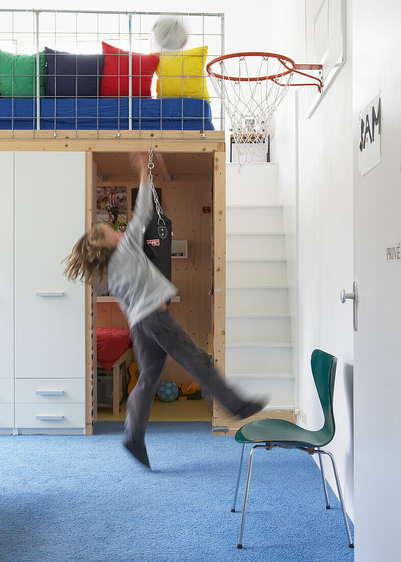 Child plays basketball in children's room with loft bed and colourful cushions