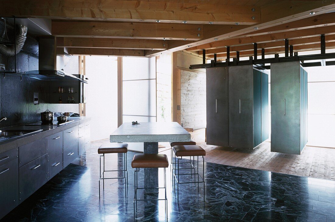 Kitchen unit and dining area with concrete table next to suspended, moveable cupboards in contemporary wooden house