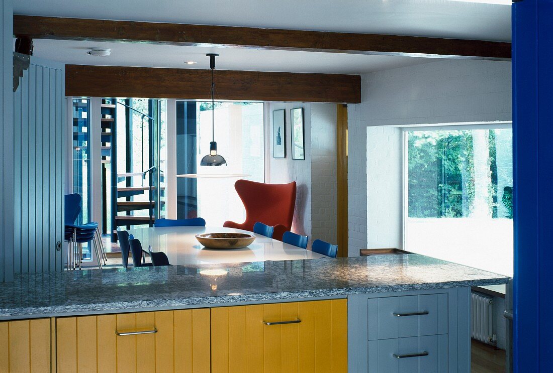 View of dining area with fifties chairs across modern kitchen unit with colourful wooden fronts and granite counter