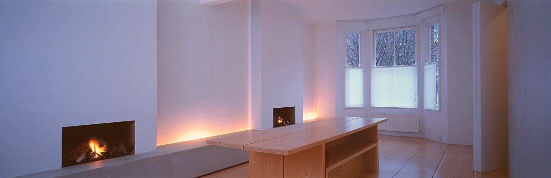 Weisser, schlichter Wohnraum mit Fenstererker und indirekter Beleuchtung zwischen zwei offenen Kaminen