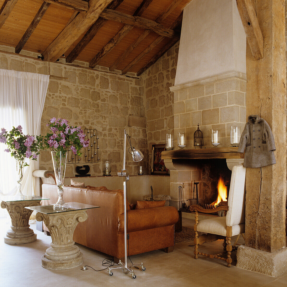 Living room with fireplace, stone wall, leather sofa and rustic wooden beams on the ceiling