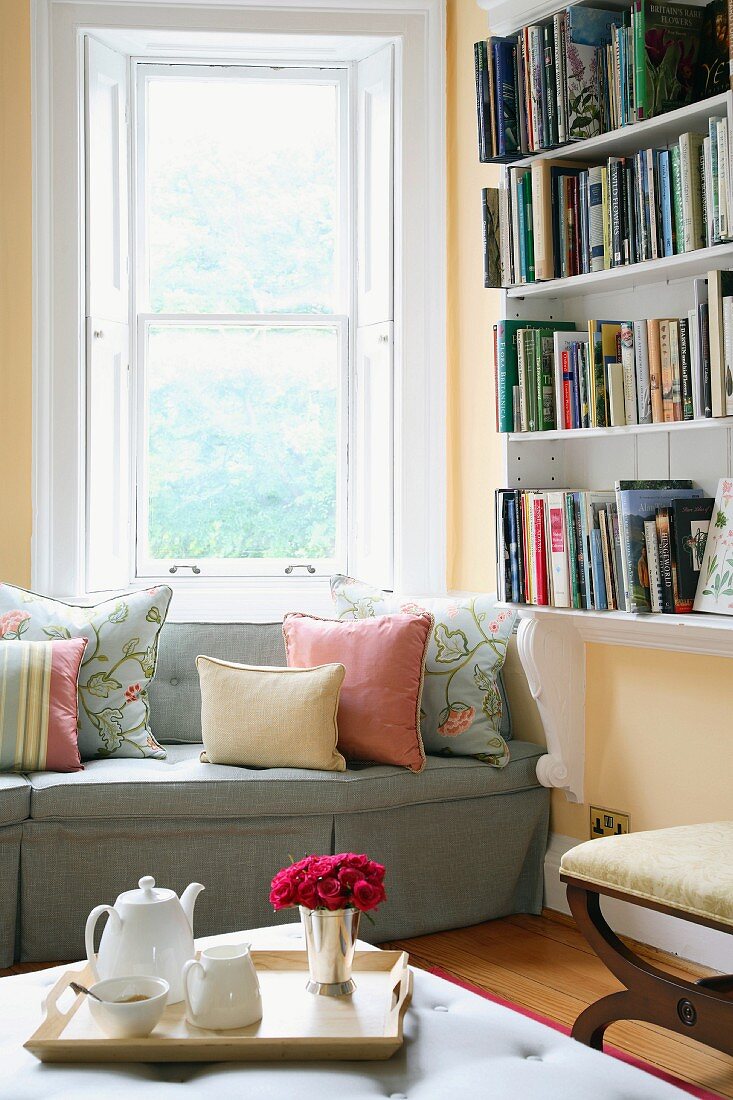 Afternoon tea in reading corner with scatter cushions on upholstered sofa and tray with posy