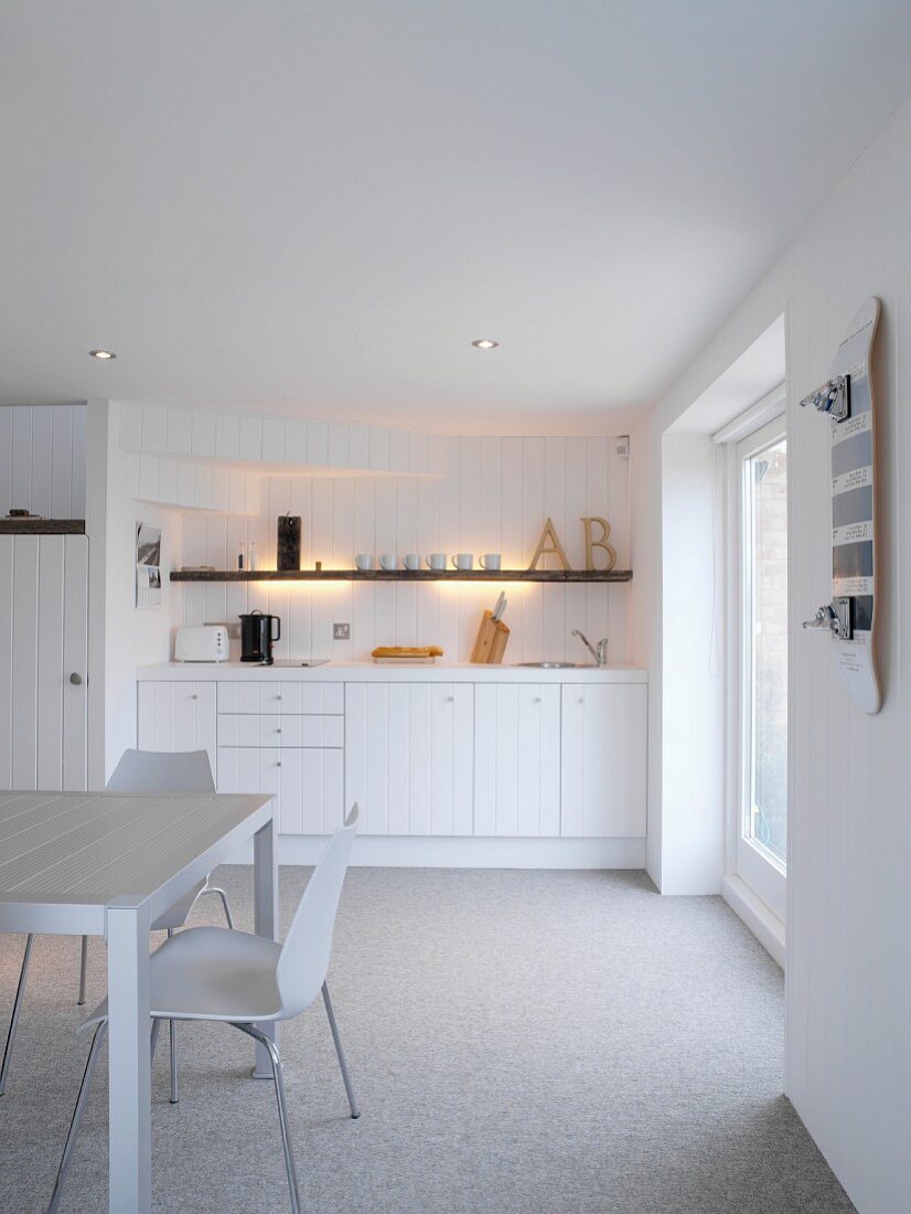 White wooden kitchen in rustic Scandinavian style with 50s chairs and skateboard on wall