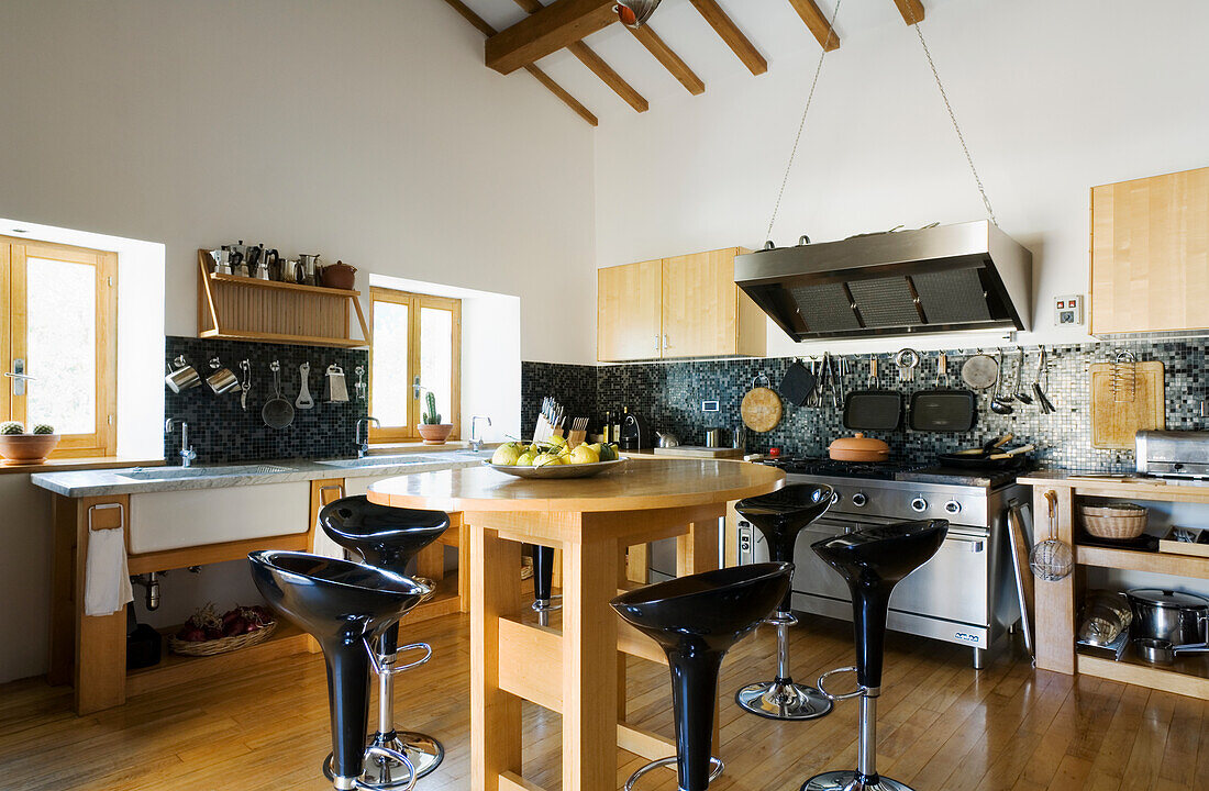 Kitchen island with black bar stools and gas hob with extractor hood