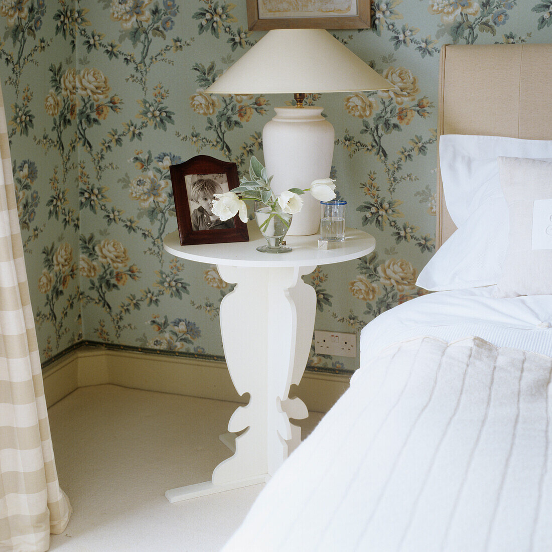 Bedside table with flowers and framed photo, floral wallpaper in the background