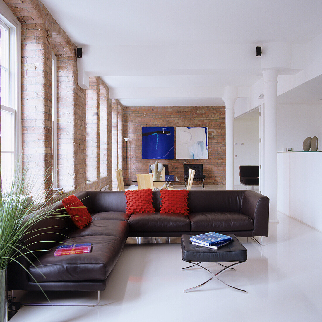 Living area with leather corner sofa and brick wall, white pillars and light-coloured floors