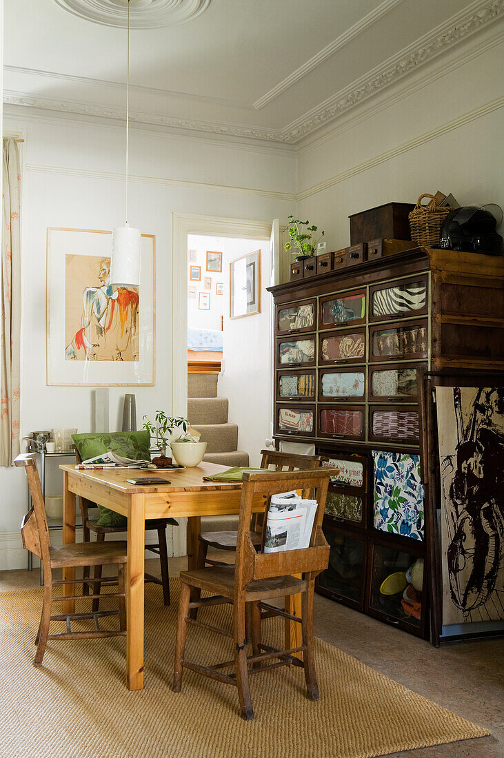 Wooden table with chairs in front of antique cupboard in dining room with staircase