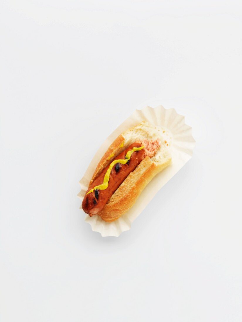 A hot dog with mustard on a paper plate with a bite taken out