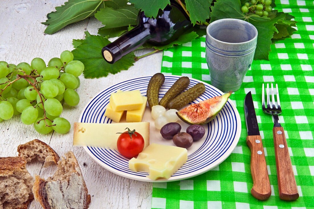 Käseteller mit Oliven, Essiggurken, Brot und Wein