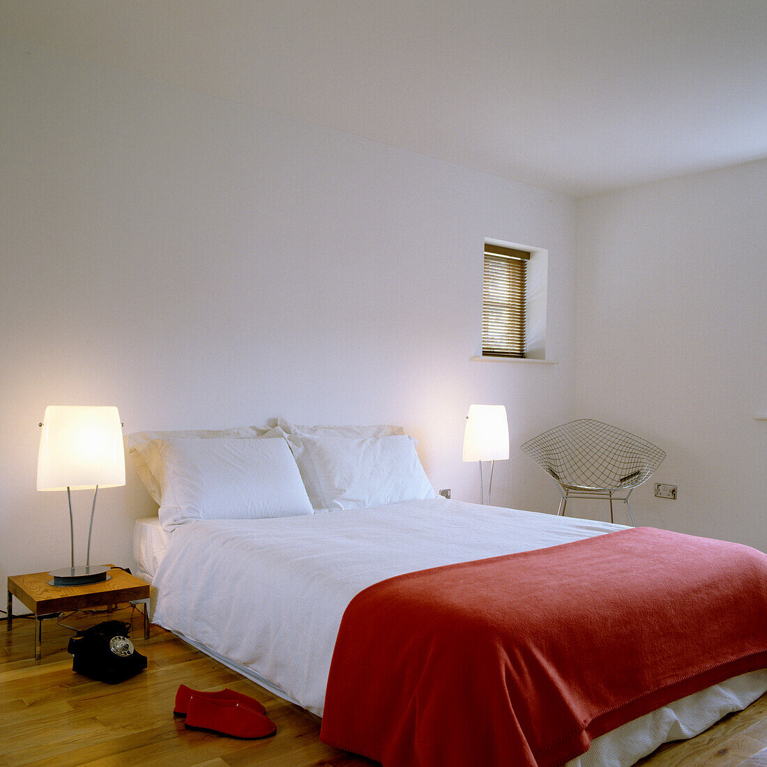 Bedroom with white bed linen and red bedspread, wooden floor and bedside table