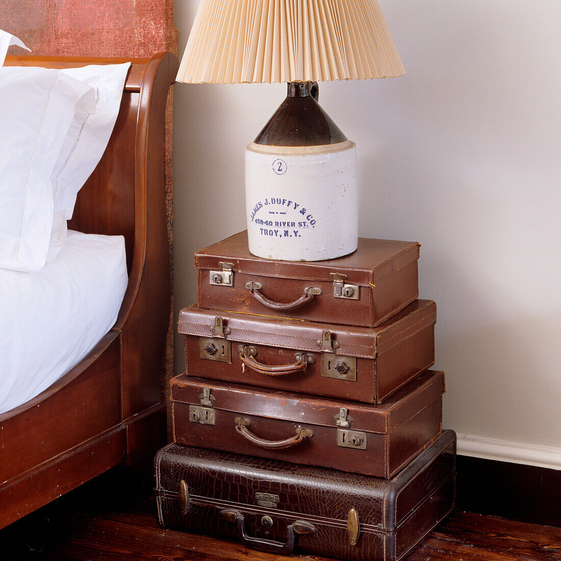 Stack of vintage suitcases as bedside table, lamp and wooden bed