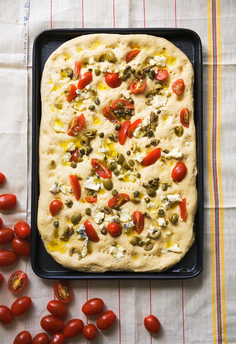 Focaccia belegt mit Tomaten, Oliven, Kapern & Käse auf Blech